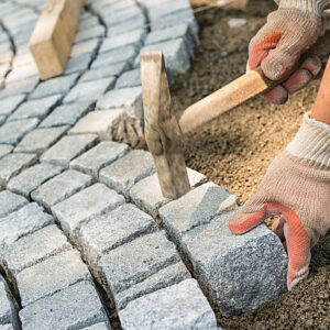 Laying paving stone, just hands in gloves and a hammer in action, hammering on the paving stones.