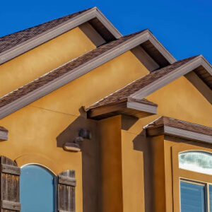 Panorama Home with concrete and stone exterior wall against clear blue sky on a sunny day. The small arched windows have rustic wooden shutters.